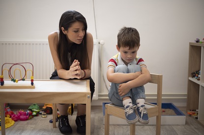 Educator sitting with a child who looks downcast with hands wrapped around their legstrying to cheer up a child