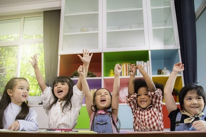 Children sitting at a table, cheering, with arms in the air