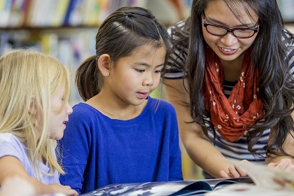 Children looking at a story book with an educator reading along with them