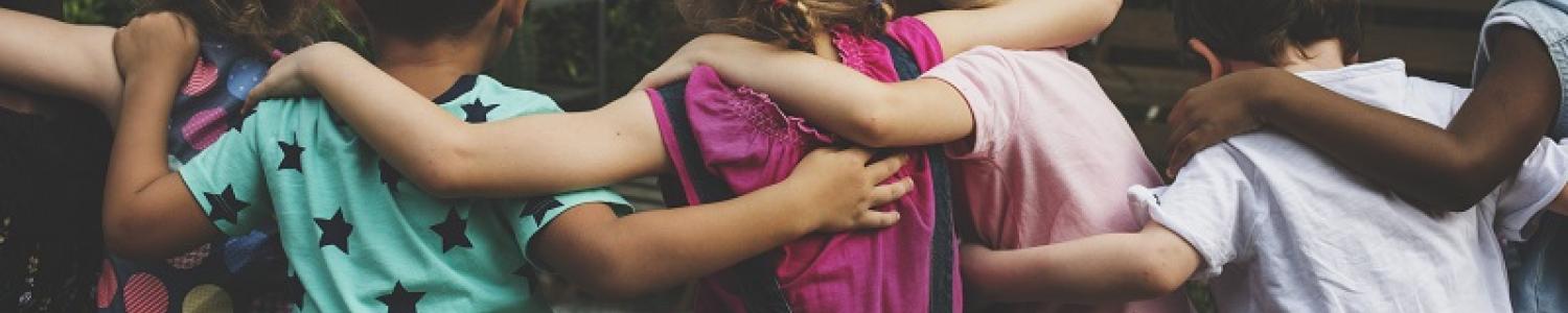 Children sitting in a row with their backs facing the camera and with arms wrapped around each other