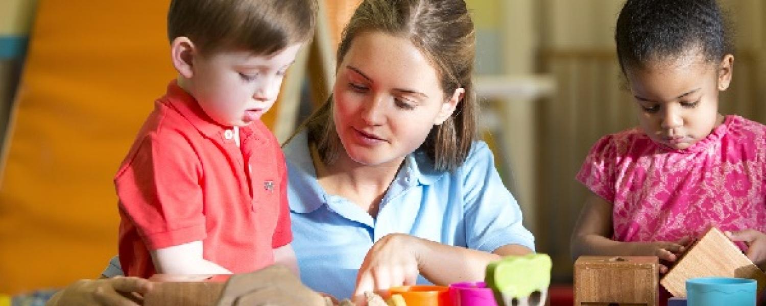 Educator and children sitting at a table and learning about blocks