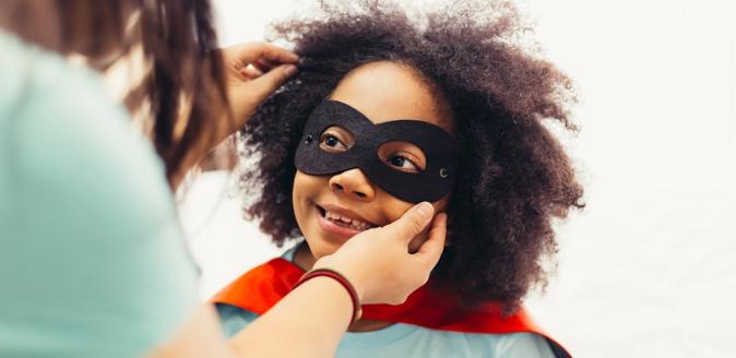 Educator helping a child put on a super hero mask