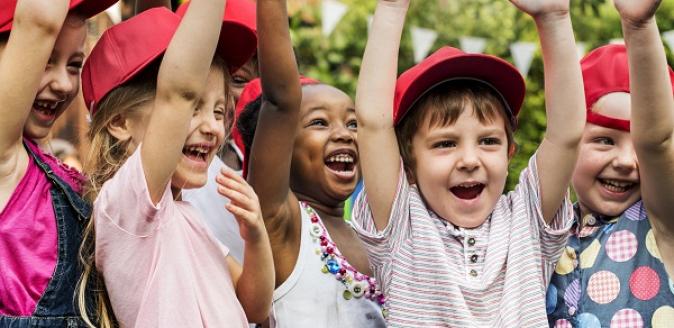 School-aged children wearing red baseball caps, celebrating with hands up in the air